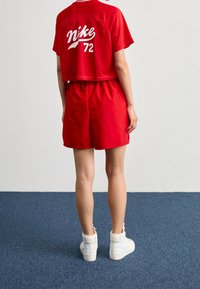 Červené crop tričko a červené šortky s bílým nápisem „Nike 72“ na zádech. Nošeno s bílými vysokými teniskami.