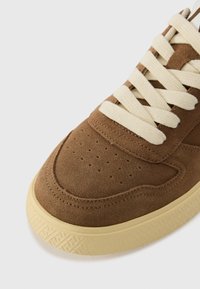 Brune semskede sneakers med kremfargede lisser, perforert tå, teksturert mellomsåle og detaljert mønster på yttersålen.