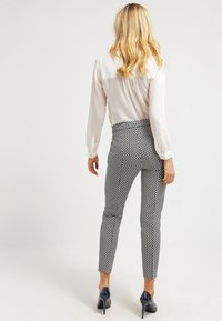 Witte blouse en zwart-wit gestreepte broek. De broek heeft een slim fit met een geometrisch patroon. Hakken maken de look compleet.