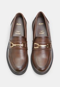 Pruun nahast loafers, millel on kuldsete metallist aksessuaaride rihm ja Ortholite'i polsterdus mugavuseks, sujuva ja poleeritud viimistlusega.