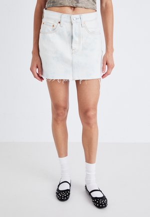 Lys blå denim mini skjørt med frynset kant, klassisk femlommers design og kontraststing. Brukt med svarte naglede leiligheter og hvite sokker.