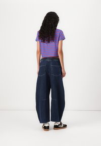 Striped, cropped top in blue and red; wide-leg, dark denim pants with a gathered waistband and two back pockets. Casual footwear completes the outfit.