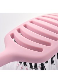 Brosse à cheveux rose ventilée avec des poils noirs surmontés de petites perles roses, présentée en gros plan sur un fond blanc.