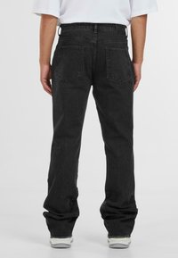 Zwarte denim jeans met een rechte pijp, zichtbare riemlussen en twee achterzakken. De stof heeft een licht gestructureerde uitstraling.