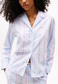 Light blue striped shirt with red vertical lines, button-up design, long sleeves, collar, and a small logo on the left chest.