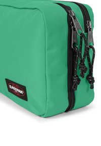 Zelený látkový sáček s dvojitými černými zipy, texturovaným povrchem, zpevněnými okraji a černou nášivkou Eastpak.