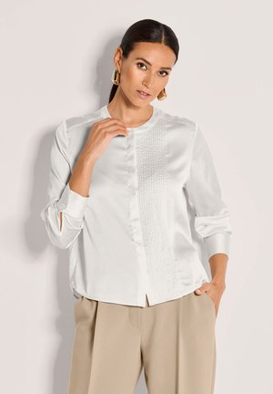 Witte satijnen blouse met een ronde hals, plooien aan de voorkant en lange mouwen. Voorzien van knopen bij de manchetten en een ontspannen pasvorm.