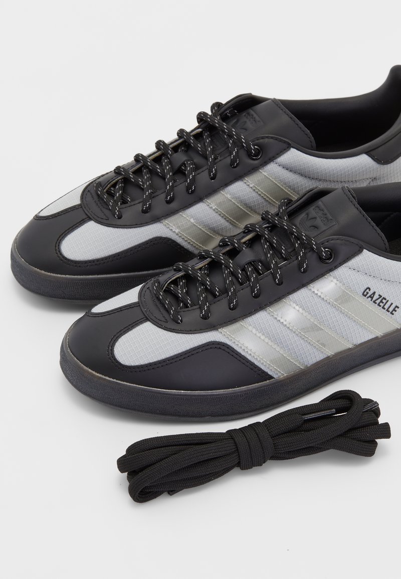 Schwarze und graue Sportschuhe mit einem Obermaterial aus glattem Leder und strukturiertem Stoff, versehen mit drei diagonalen Streifen und schwarzen Schnürsenkeln. Inklusive schwarzer Schnürsenkel.
