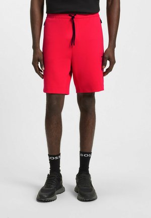 Shorts de sport rouges avec une taille à cordon, poches latérales et une finition texturée. Portés avec des baskets noires et des chaussettes de marque "BOSS".