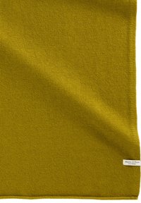 Morbido tessuto a maglia verde oliva con una piccola etichetta bianca nell'angolo in basso a destra con la scritta "Marc O'Polo EST. IN STOCKHOLM".