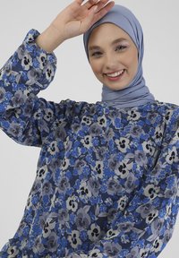 Luźna niebieska bluzka w kwiaty z długimi rękawami, z odcieniami niebieskiego, szarego i czarnego. Miękka tkanina z falbankami na końcu.