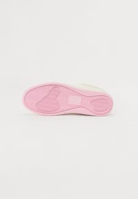 White sneaker sole with a zigzag tread pattern. The outsole is light pink, featuring a rectangular logo and rounded edges for grip.