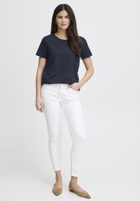 Tmavě modré bavlněné tričko s krátkými rukávy, doplněné bílými úzkými kalhotami. Boty jsou béžové baleríny se špičatou špičkou.