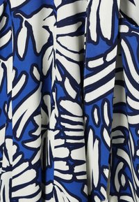 Blåt stof med hvide og mørkeblå abstrakte, uregelmæssige bladlignende mønstre og bløde lodrette folder.