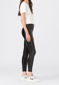 Svarta högmidjade leggings i mjukt, stretchigt material, tillsammans med en kortärmad vit topp och kraftiga vita sneakers.