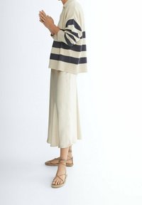 Beżowy sweter w paski z granatowymi paskami, połączony z kremową spódnicą maxi i beżowymi sandałami na paski. Miękkie tkaniny o luźnym kroju.