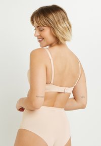 Reggiseno color nude e mutandine a vita alta realizzate in tessuto morbido. Il reggiseno ha spalline regolabili e una chiusura con gancio e occhiello sul retro.