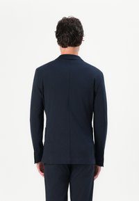 Blaser azul marinho com uma textura suave, corte ajustado, abertura traseira única e dois bolsos laterais. Design simples, adequado para vestuário formal.