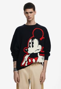 Sort strikket sweater med et stort rødt og hvidt Mickey Mouse-design på forsiden. Rund halsudskæring og løse ærmer.