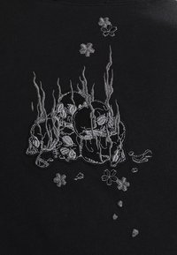 Czarny T-shirt z materiału z haftowanymi srebrnymi czaszkami, płomieniami i kwiatami. Szczegółowe przeszycia dodają tekstury i kontrastu wizualnego.