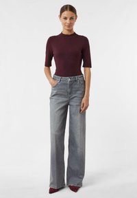 Burgundy ribbed knit top with short sleeves paired with high-waisted, loose-fit gray jeans. Model stands with hands in pockets.
