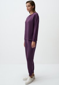 Paars comfortabel sweatshirt en een bijpassende tapered broek, gemaakt van zacht materiaal. Witte sneakers maken de casual outfit compleet.