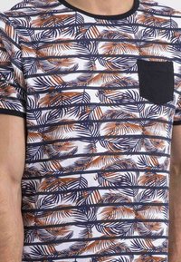 Chemise à manches courtes avec une base blanche, ornée de motifs de feuilles de palmier orange et marine, et d'une poche poitrine unie marine. Matière en mélange de coton.