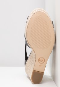 Semelle d'une sandale compensée Michael Kors avec talon en jute tressé et tige en cuir noir, taille 8M, positionnée verticalement contre une surface blanche.