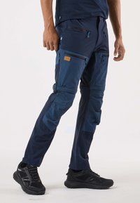 Marinblå vandringsbyxor med flera fickor med dragkedja, tillverkade av ett hållbart material. Har en kontrasterande ljusare blå panel och en logotypmärke.