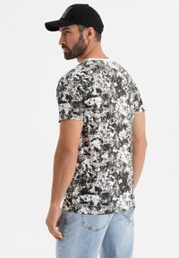 Tričko s krátkým rukávem vyrobené z bavlny, s černobílým skvrnitým vzorem. Kulatý výstřih a slim fit střih.