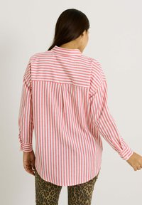 Camisa de rayas rojas y blancas de mangas largas con cuello y detalles de pliegues en la parte posterior. Combinada con pantalones estampados de leopardo texturizados.