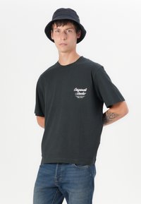 Black cotton t-shirt with short sleeves and a crew neck. Features white printed text on the left chest. Paired with blue denim jeans.
