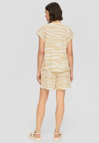 Beige Kurzarmoberteil und passende Shorts mit einem weißen Zebra-Streifen-Muster, aus leichtem Stoff gefertigt. Sandalen mit Knoten-Detail.