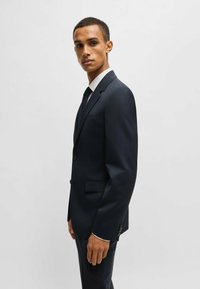 Abito navy a righe sottili in tessuto leggero, caratterizzato da un blazer a un bottone e pantaloni slim fit, con una leggera lucentezza e dettagli sartoriali.