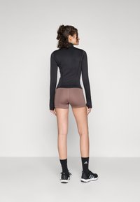 Svart langermet treningsgenser kombinert med brune shorts. Glatt stoff, høy hals og kontrasterende sideaksenter. Svart treningssko og sokker.