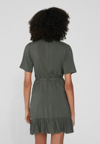 Robe vert olive avec des manches courtes, taille cintrée et ourlet volanté. Fabriquée en tissu lisse, avec un dos épuré.