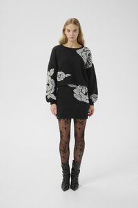 Zwart gebreid sweater met grijze bloemenpatronen, gecombineerd met een zwarte aansluitende rok en doorschijnende panty’s met bloemenontwerpen, aangevuld met zwarte kniehoge laarzen.
