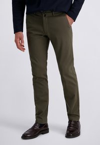 Olijfgroene slim fit broek van gladde stof. Beschikt over voorzakken en riemlussen, gecombineerd met donkerbruine instapschoenen.