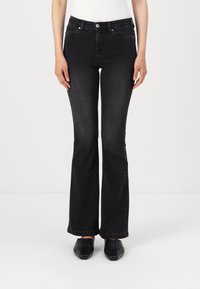 Jeans neri a palazzo con una texture liscia, vita alta, tasche anteriori e chiusura con bottone. Indossati con scarpe nere senza lacci.