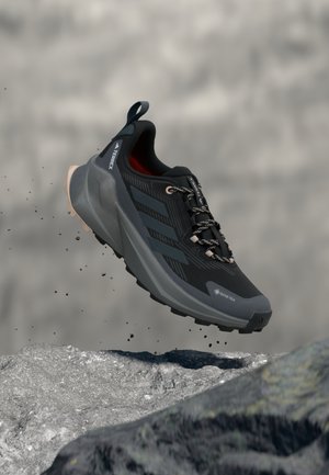 Chaussure de randonnée noire avec tige texturée, accents gris et semelle extérieure robuste. Éléments réfléchissants et détails de lacets. Marque GORE-TEX visible.