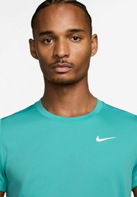 Camiseta deportiva turquesa con cuello redondo y mangas cortas, que presenta un logo de Nike en blanco en el pecho. Tejido suave y ajustado.