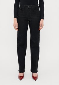 Fekete farmer egyenes szabású nadrág, öt zsebbel, diszkrét varrással és közepes derékkal, piros lakkbőr magassarkú cipővel párosítva.