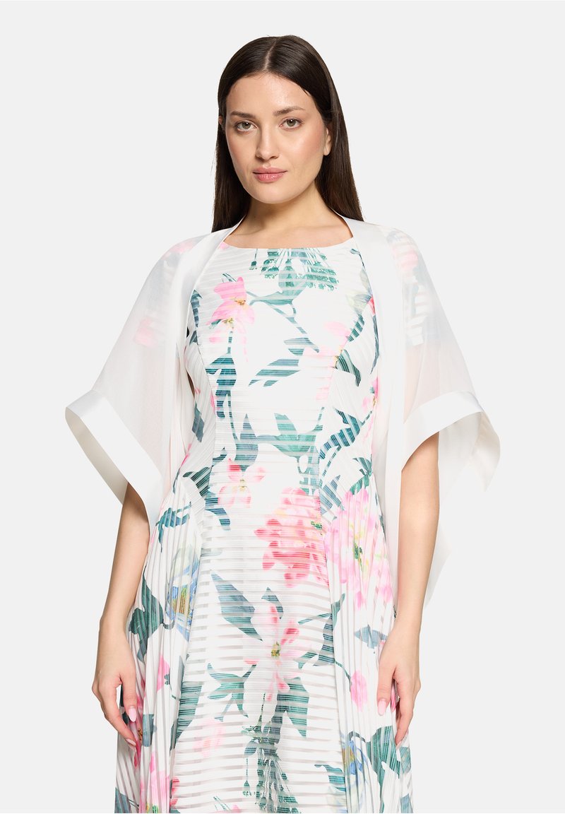 Blumenkleid mit pinken und grünen Mustern, plissierter Struktur und einer weißen, transparenten Jacke mit offenem Vorderteil.