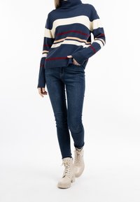 Merensininen ja kerma raidallinen pooloneule, jossa on ribbineulos, yhdistetty kapeisiin sinisiin farkkuihin ja beigeihin nauhallisiin nilkkureihin.