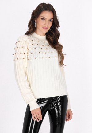 Cremefarvet strikket sweater med ribbet tekstur, der har en mønstret øverste sektion prydet med guldperler og en høj hals.