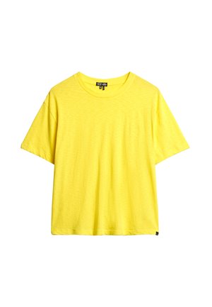 Helles gelbes T-Shirt mit kurzen Ärmeln und Rundhalsausschnitt, das eine feine Struktur aufweist und einen kleinen schwarzen Anhänger am Saum hat, vor einem weißen Hintergrund.