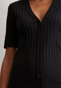 Cárdigan negro de punto acanalado con un profundo escote en V, mangas cortas y una fila de cinco botones negros en el frente para su cierre.