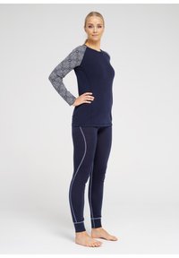 Mørkeblå sportsbluse med mønstrede grå ærmer, parret med matchende tætsiddende leggings med en kontrasterende lysegrå søm.