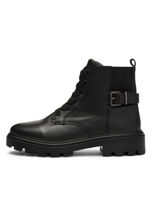 Black leather combat boot with thick lug sole, front laces, ankle strap with metal buckle, and pull tab at back.