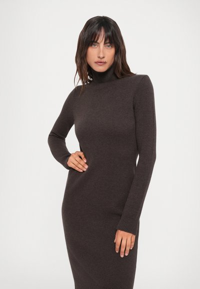 Rochie tricotată cu guler înalt, de culoare maro închis, având mâneci lungi și o siluetă ajustată cu manșete cu nervuri. Țesătură netedă, texturată.